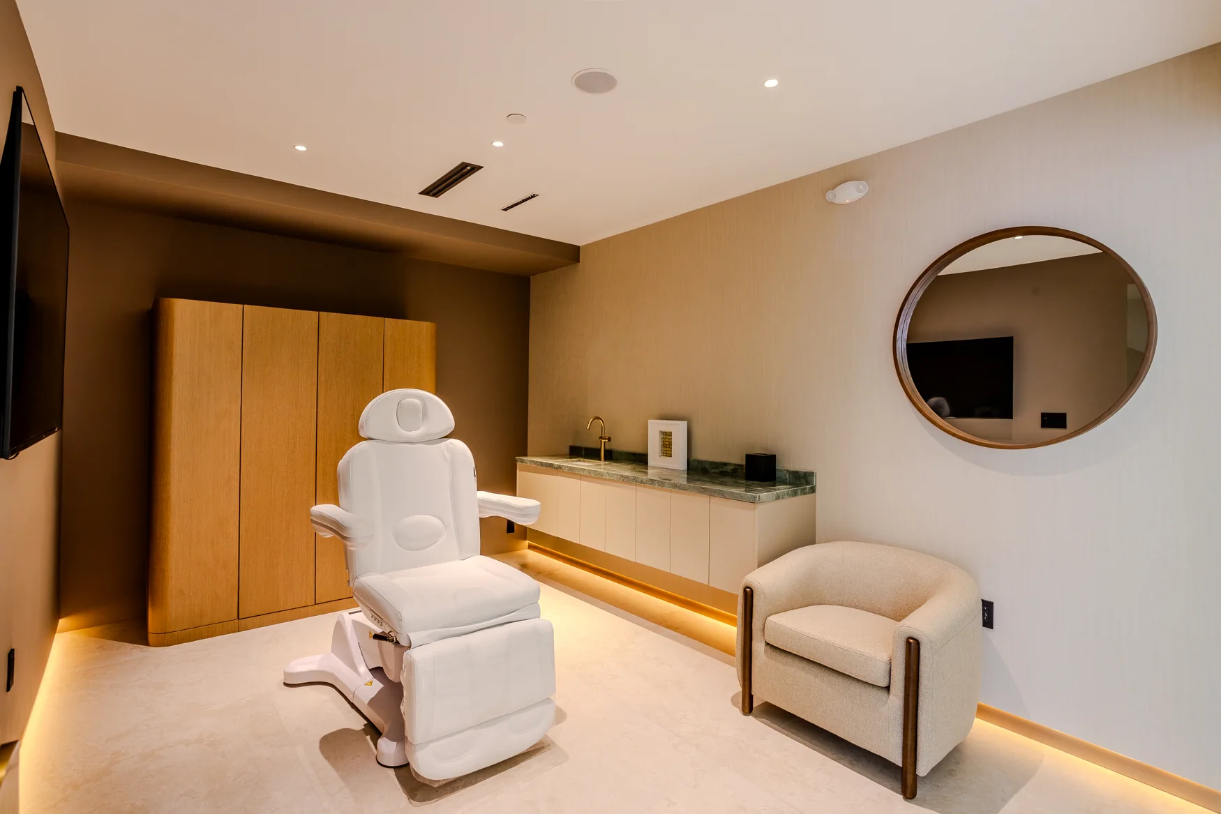 White adjustable chair, cream armchair, wooden cabinet and circular wall mirror.