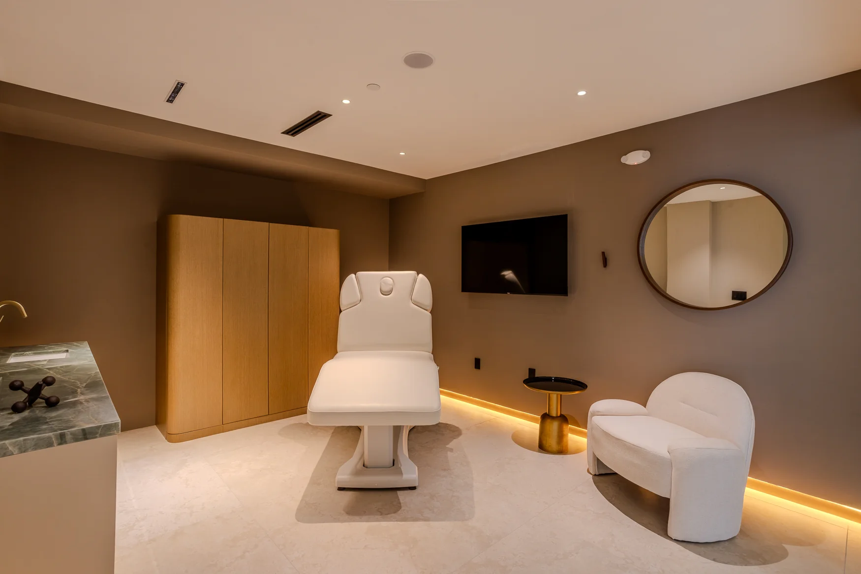 Front view of a white adjustable chair with a circular mirror and cream armchair to the side.