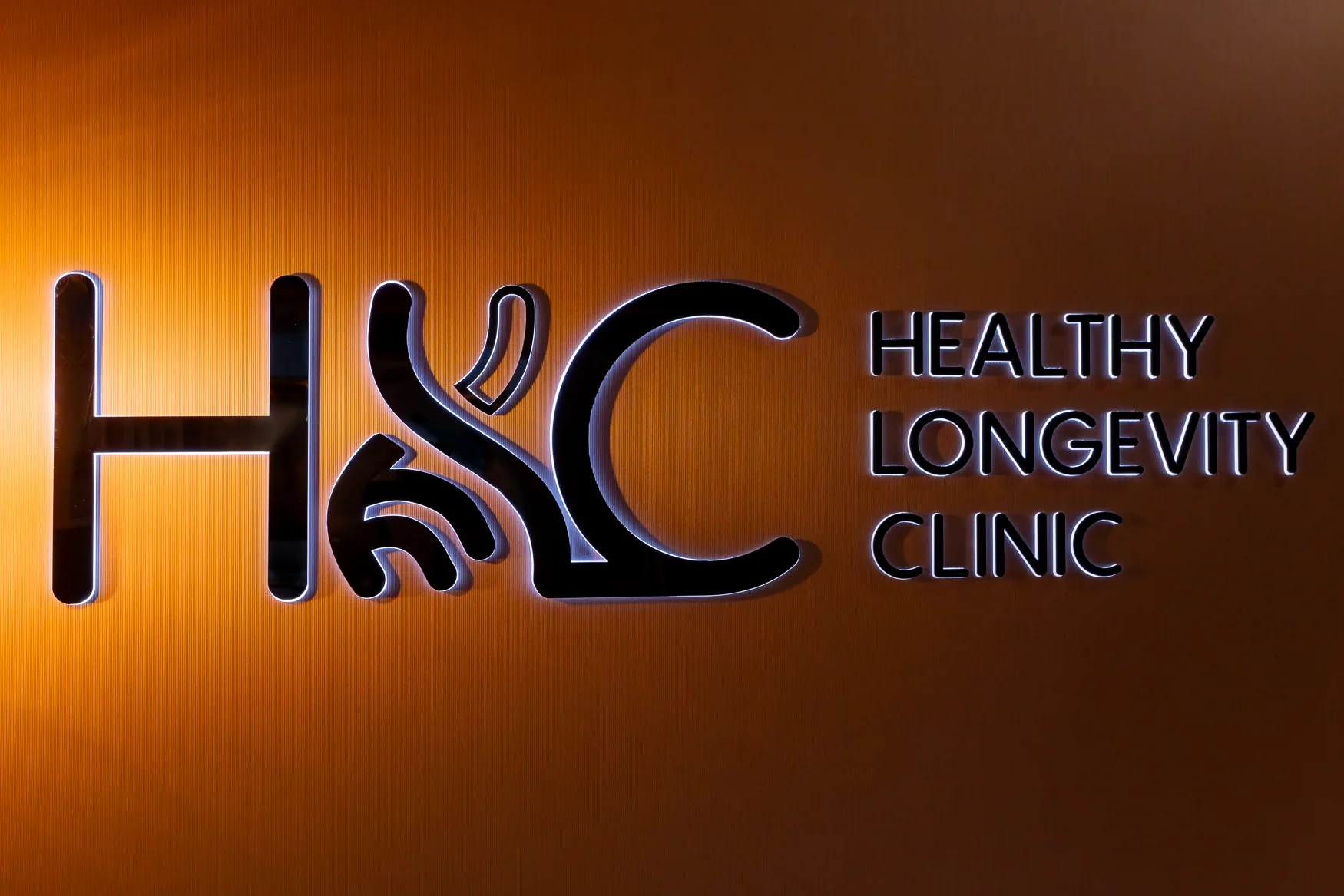 Illuminated HLC Healthy Longevity Clinic lettering on a warm-toned wall.
