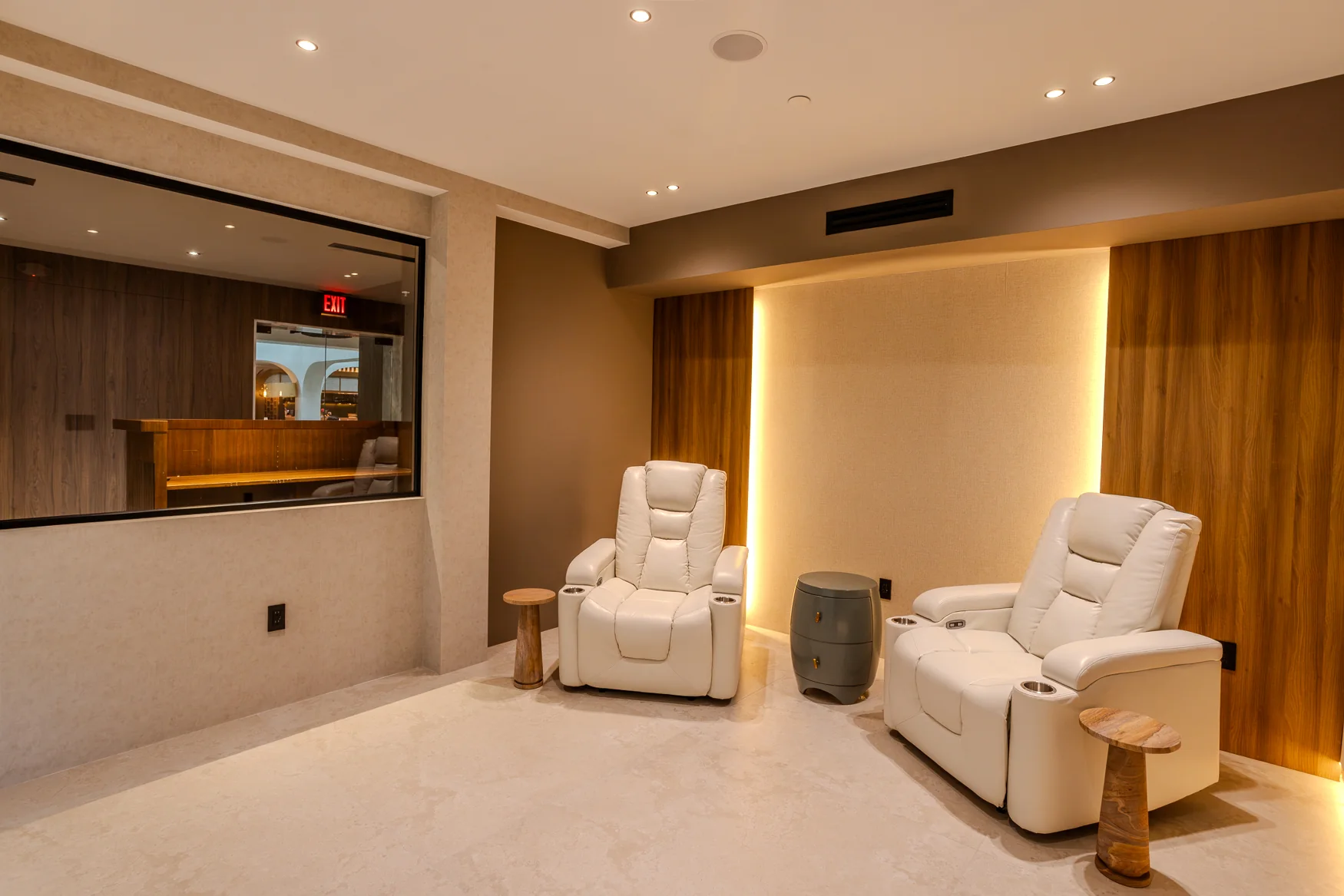 Two white reclining chairs with small side tables against illuminated wood panels.