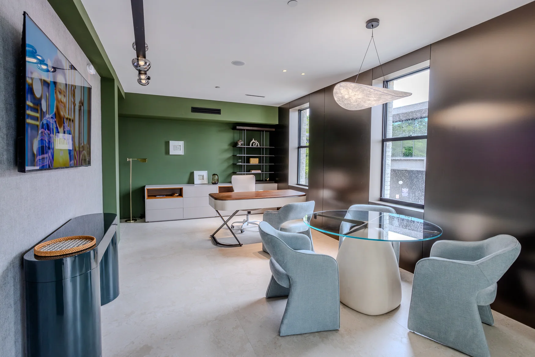 Green-accented room with a desk, glass conversation table, upholstered chairs and a window.