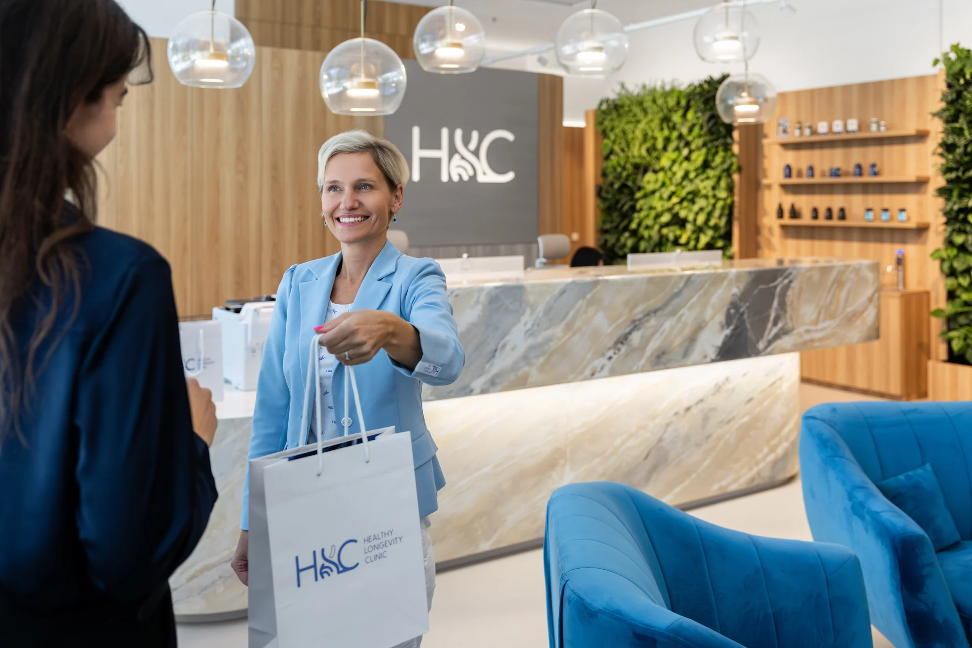 A woman in a light blue jacket handing an HLC bag to another woman at reception.